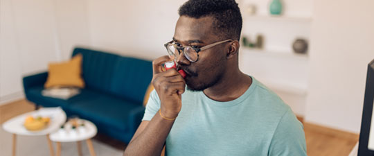 young African American man using asthma inhaler at home