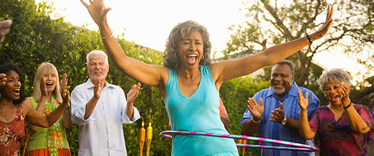 Happy woman using a hula hoop in front of a crowd of laughing and cheering friends. 