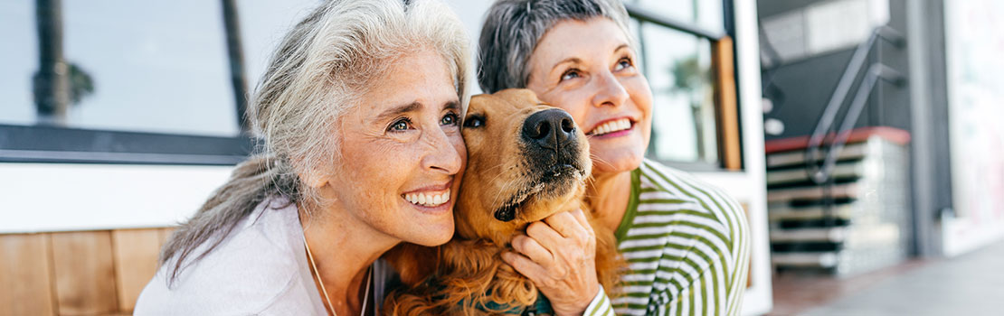 Two senior women snuggling outside with dog
